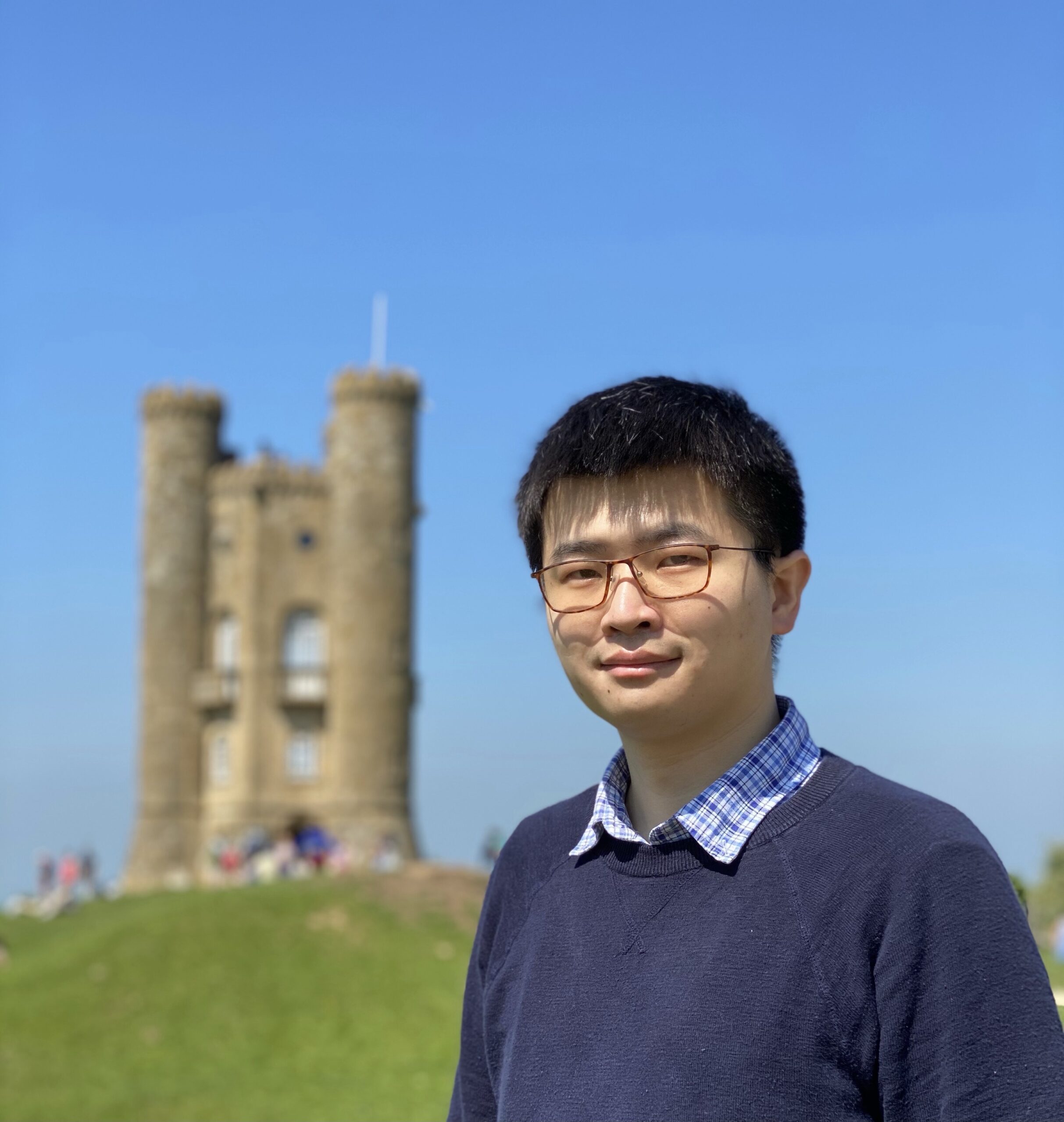 Professor Wang against a blue sky, wearing a blue collared shirt and blue sweater