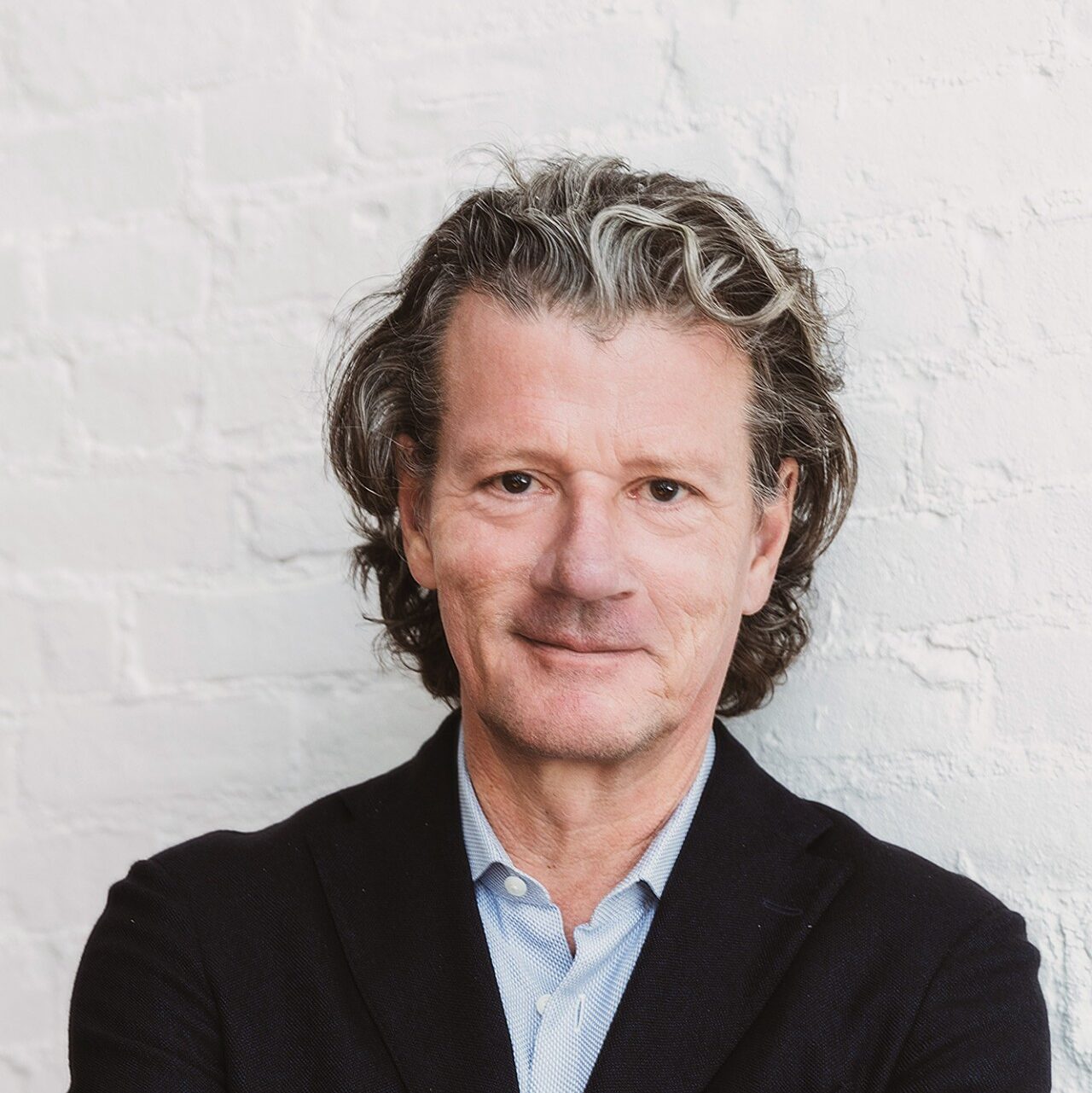 Professor Wimmer wearing a black coat with a blue shirt standing against a white background